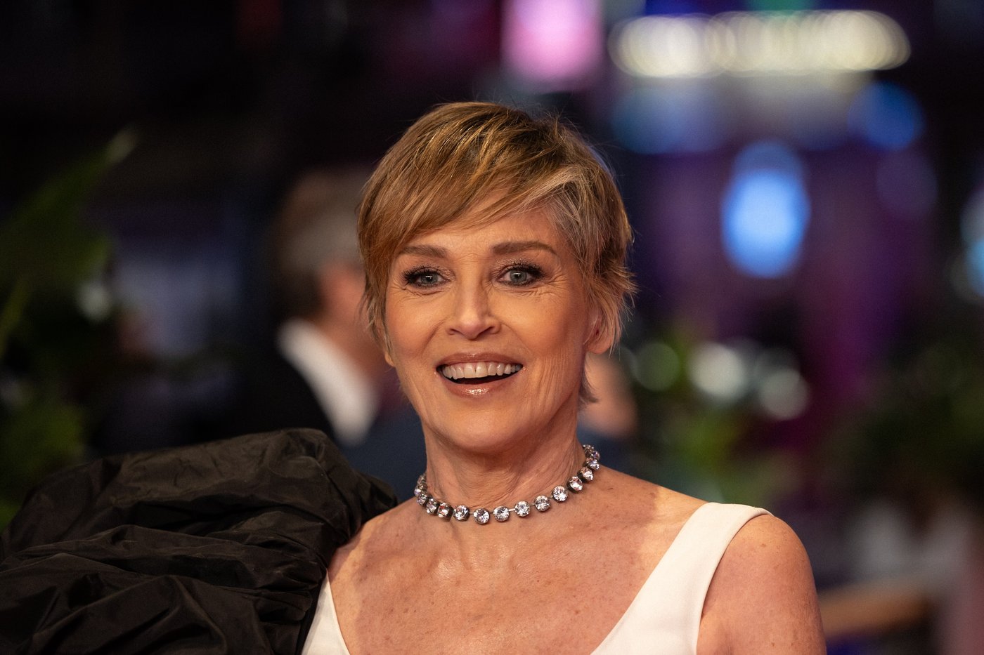 Sharon Stone smiling in a white dress and diamond necklace in February 2024