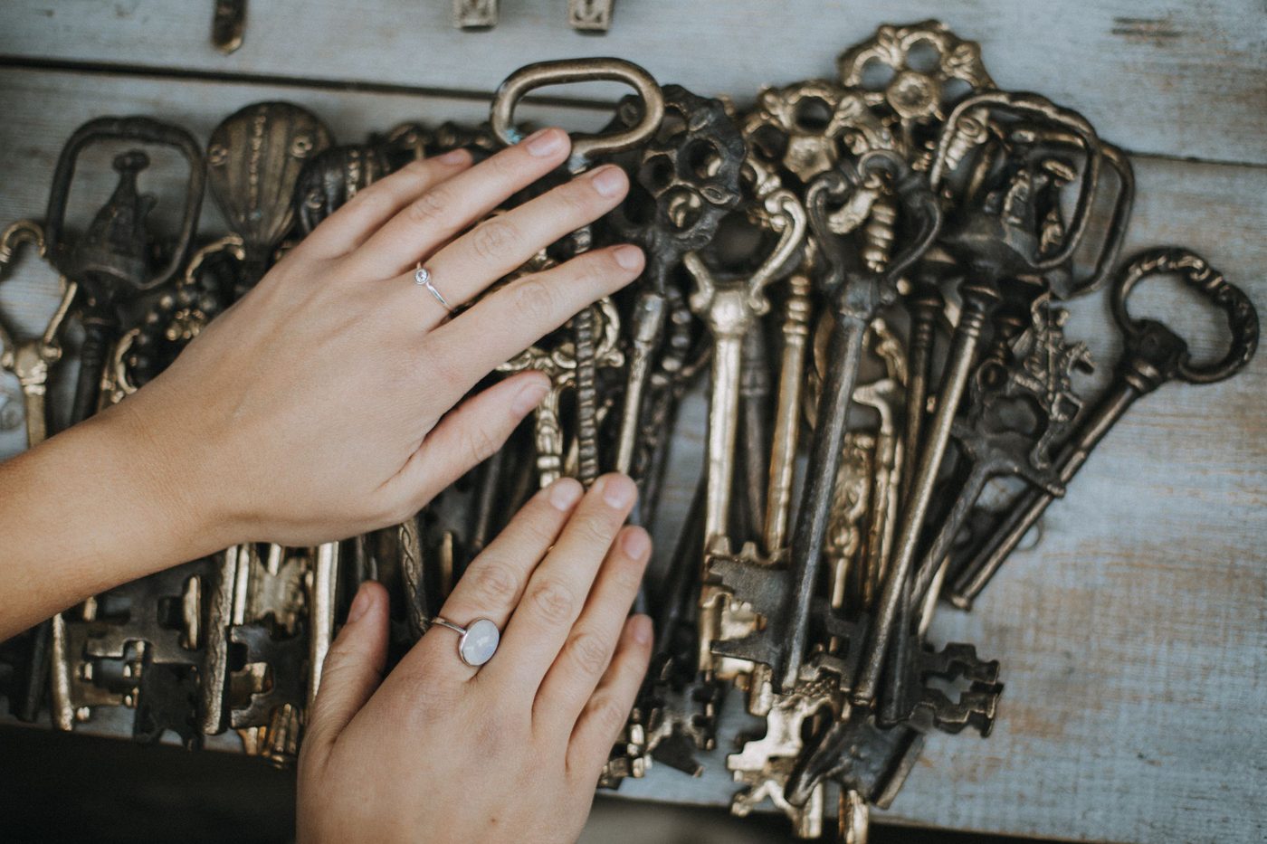Two hands sorting through a pile of old iron keys on a weathered table