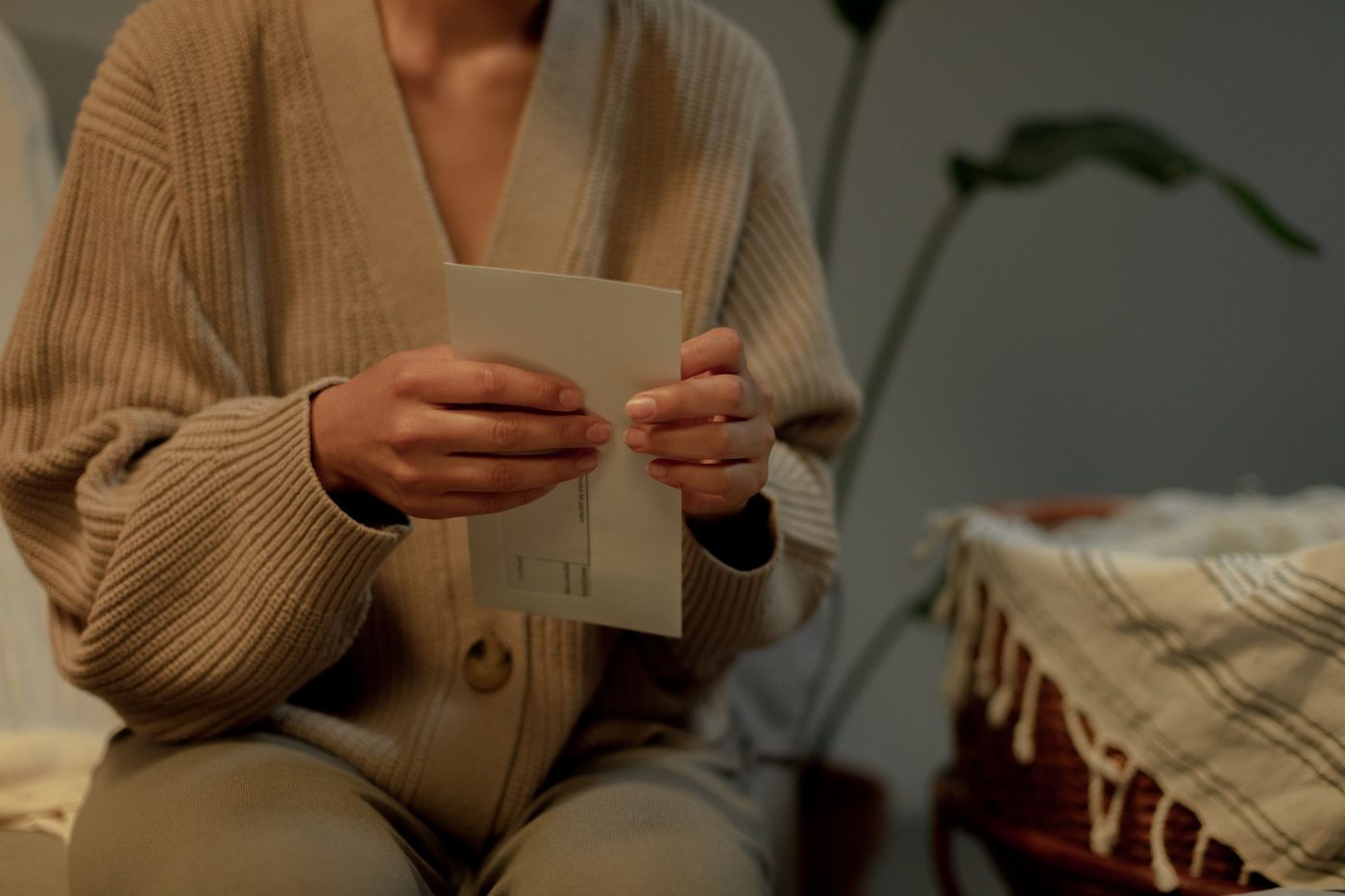 A person in a warm knitted cardigan holds an opened envelope with a folded letter
