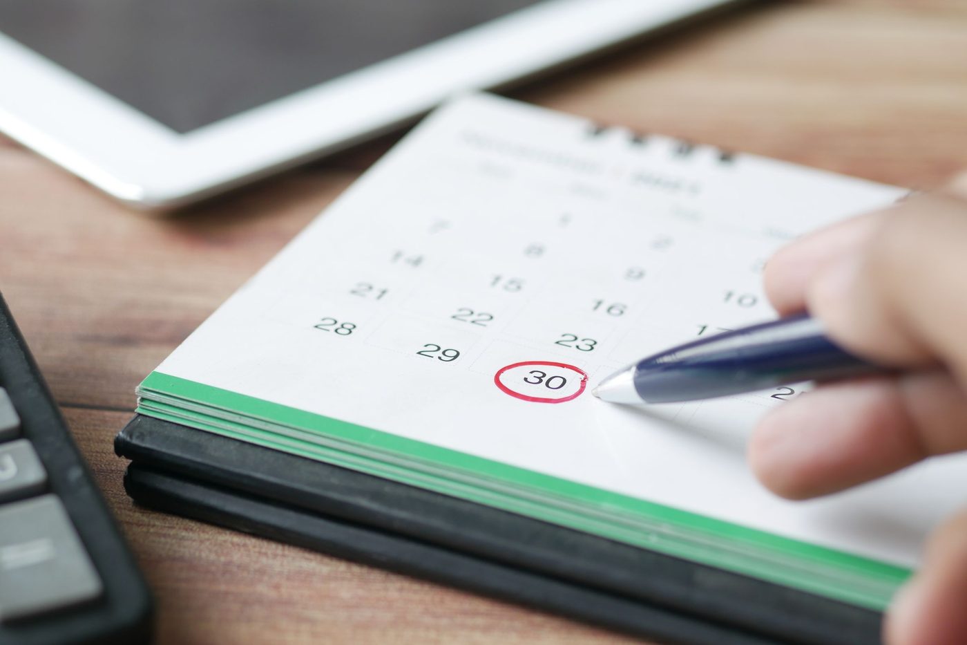 A hand circles the 30th on a desk calendar with a blue pen