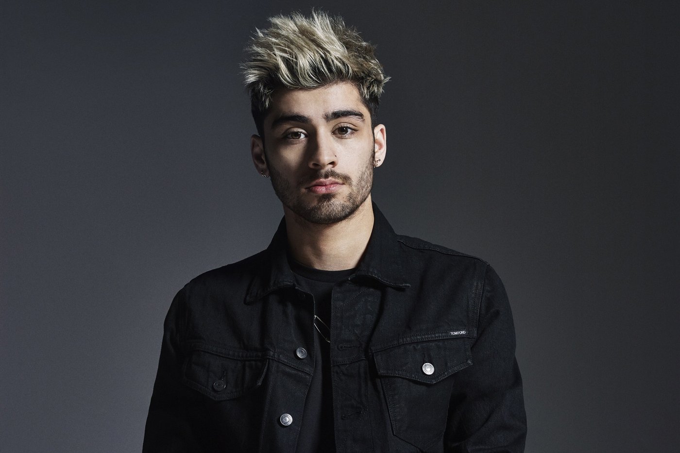 Zayn Malik in black denim against a grey studio backdrop in 2015