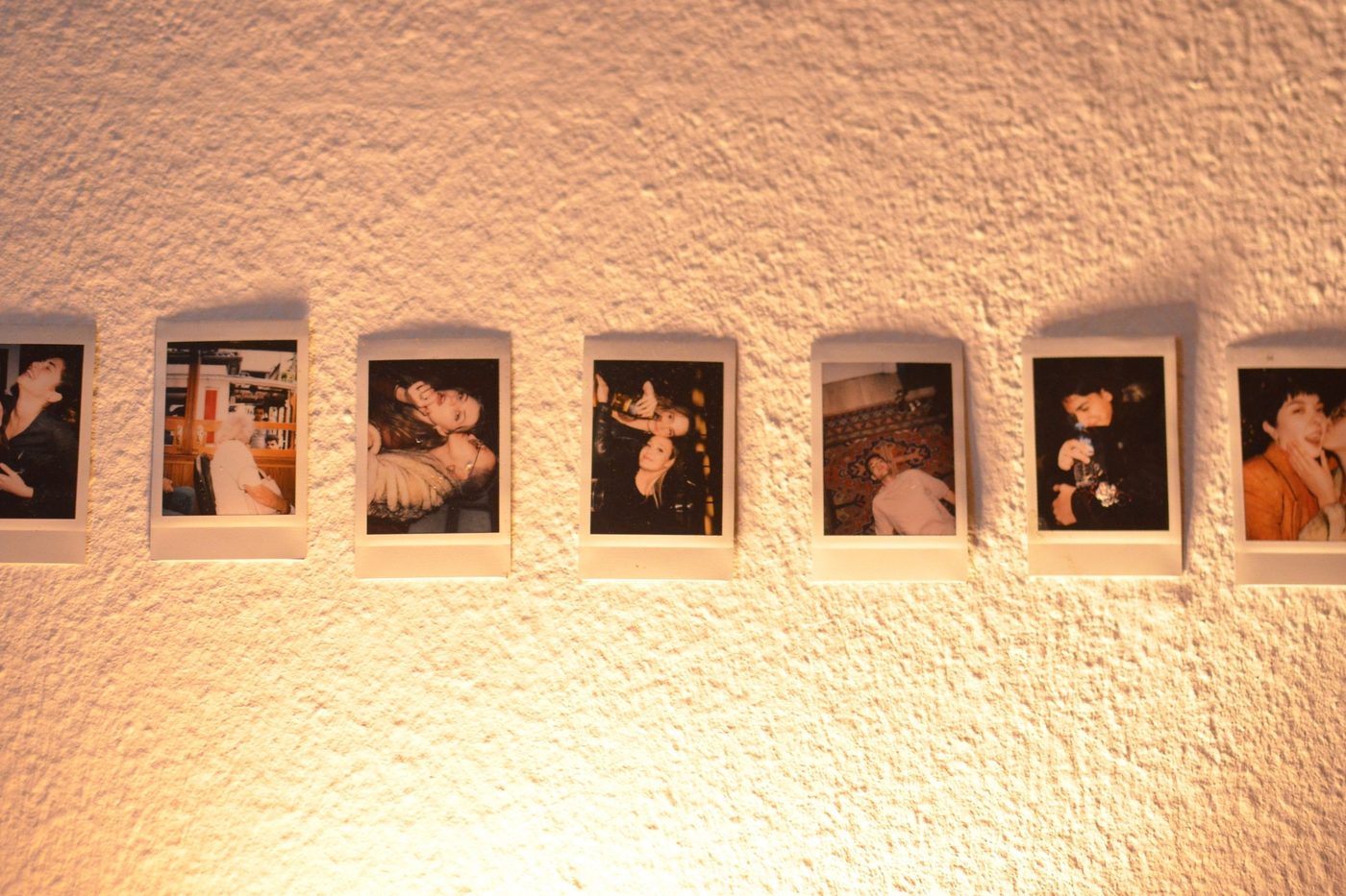A row of instant photo prints of people pinned in a line on a warmly lit wall