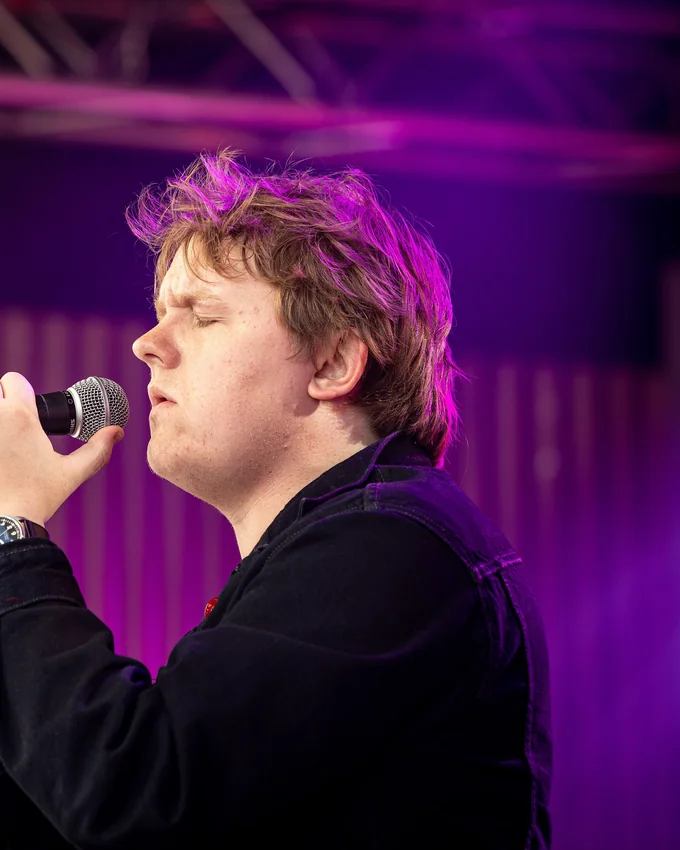 Lewis Capaldi singing under purple stage lights in 2019
