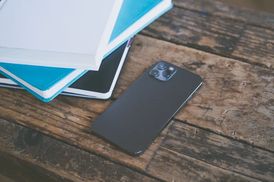A dark smartphone lies face down beside a stack of notebooks on a rustic wooden table