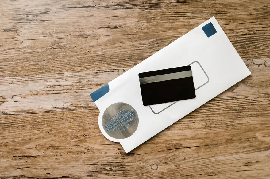 The back of a bank card with a dark magnetic stripe lies on a white envelope on a wooden table